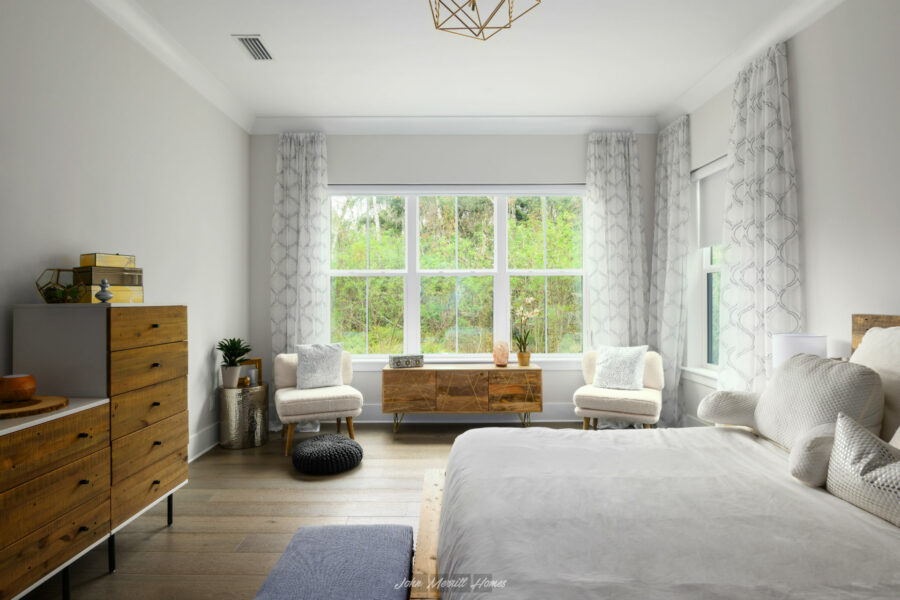 Modern bedroom with large window, white walls, light wood flooring, and contemporary furniture including a bed, dresser, armchairs, and decorative accents, creating a cozy and stylish space.