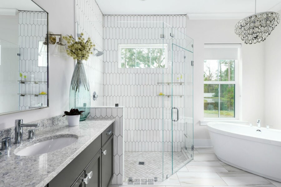 Bright modern bathroom with a glass-enclosed shower, freestanding bathtub, and elegant vanity with a granite countertop, featuring large windows and contemporary lighting fixtures.