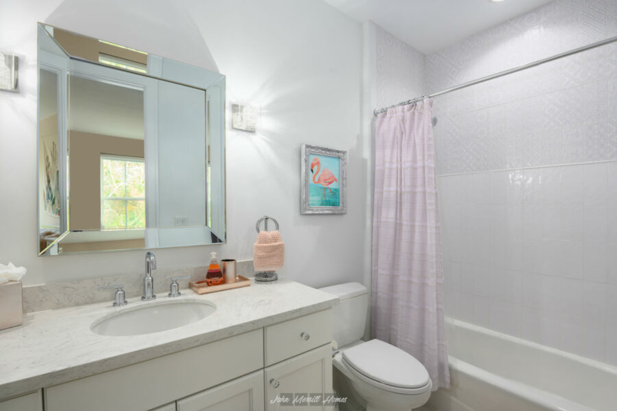 Reflective bathroom vanity mirror with modern fixtures, pink flamingo artwork, and a comfortable shower and tub combo with a light pink shower curtain in a bright, white bathroom.