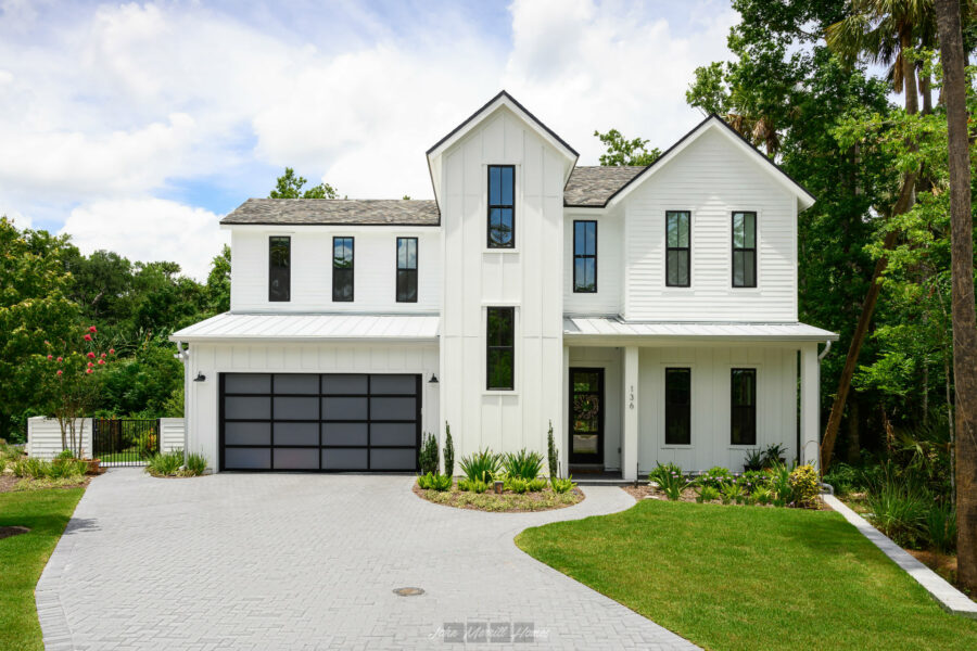 Modern white farmhouse-style home with black accents, large windows, and a landscaped front yard with a curved brick driveway.