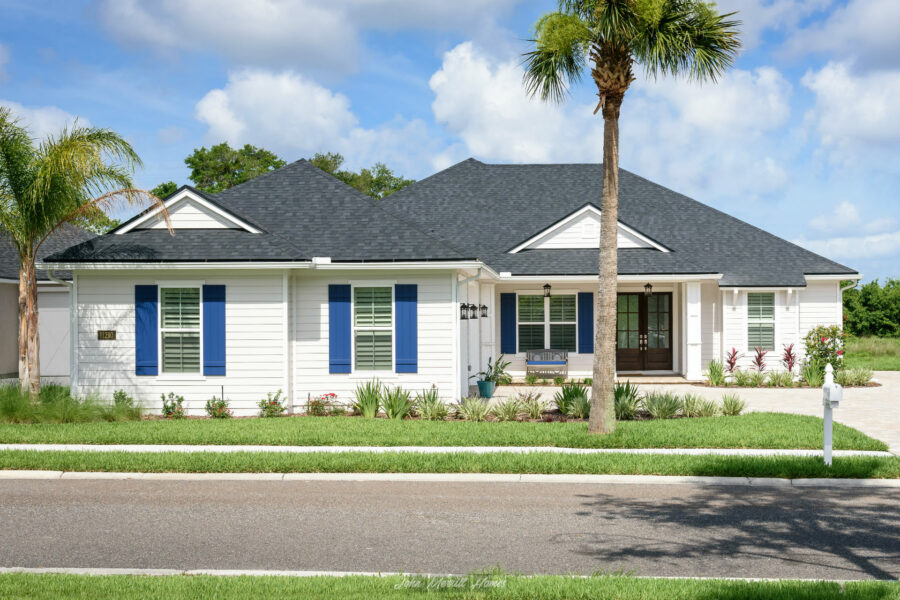 Modern white single-story home with black roof, blue shutters, and lush landscaping, showcasing quality construction and curb appeal.