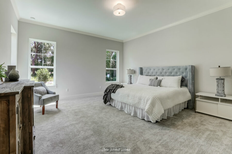 Spacious modern bedroom featuring a large bed with a tufted headboard, soft neutral tones, and large windows providing ample natural light, creating a serene and comfortable retreat.