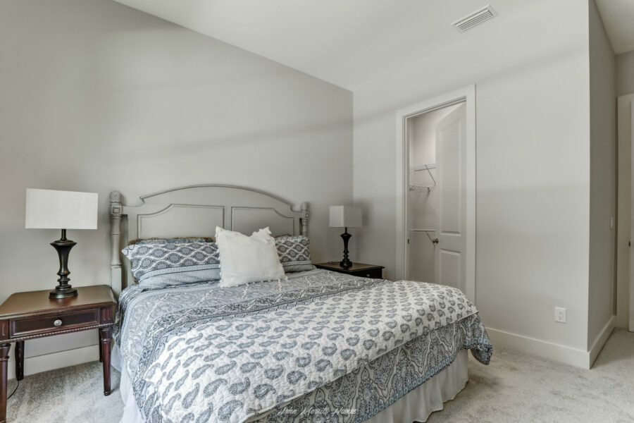 Spacious bedroom with a neatly made bed, patterned bedding, two side tables with lamps, white walls, and a closet in the background.