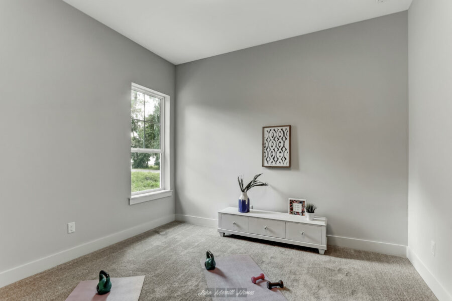 Modern minimalist home exercise room with neutral decor, white TV stand, wall art, and yoga mats with weights for fitness. Bright natural light from a window highlights the cozy, contemporary space.