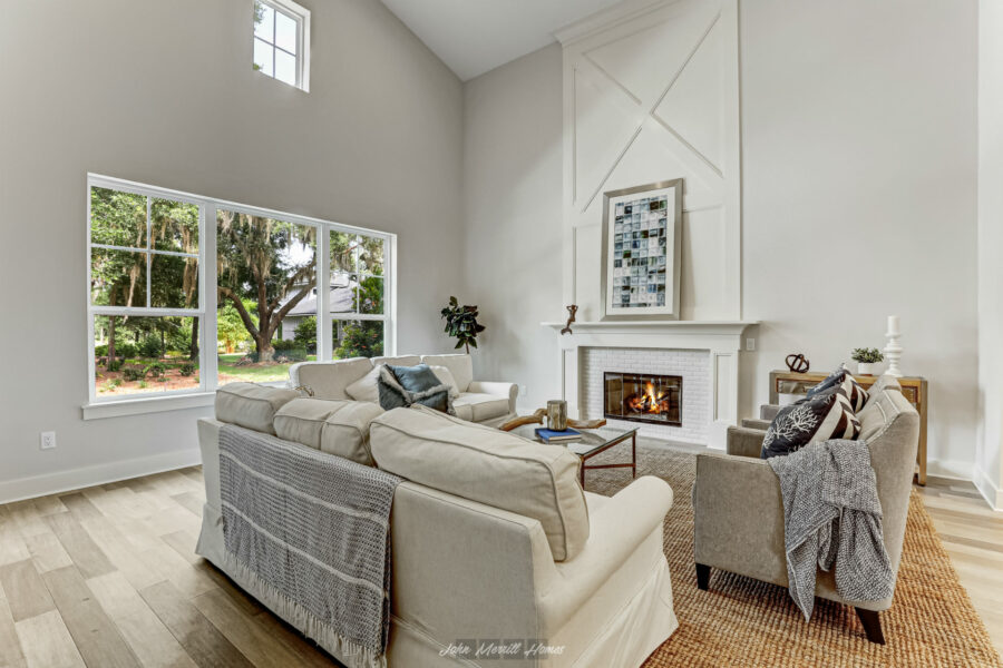 Modern living room with a cozy fireplace, large windows showcasing lush outdoor greenery, and stylish furniture creating an inviting atmosphere | Bright, airy open-concept space with high ceilings, white walls, and natural light | Image of a contemporary home interior emphasizing comfort and elegance, perfect for relaxing or entertaining guests.