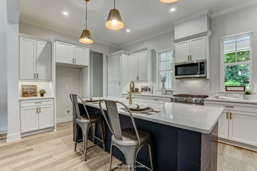 Bright modern kitchen with white cabinets, marble countertops, a navy blue island, stainless steel appliances, and large windows bringing in natural light. Perfect for cooking and gathering.