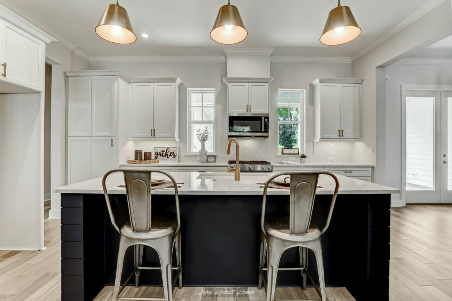 Modern white kitchen with a large island, pendant lighting, stainless steel chairs, and bright natural light from the windows, showcasing elegant cabinetry and contemporary design.