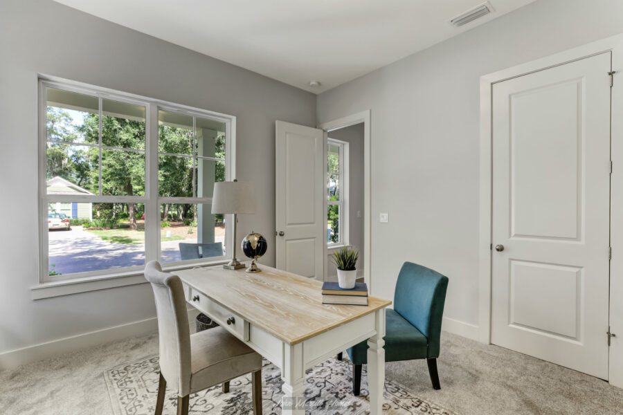 Bright home office with large windows, white walls, light-colored furniture, and a view of a peaceful neighborhood outside.