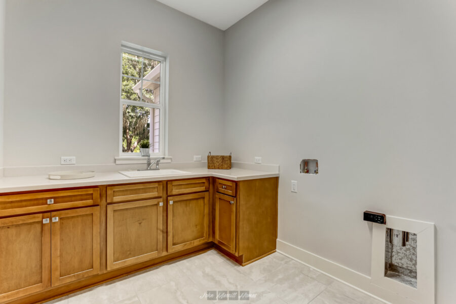 Brand new kitchen with wooden cabinetry, a white countertop, and a window overlooking a leafy yard, designed for modern living with ample space for appliances and natural light.