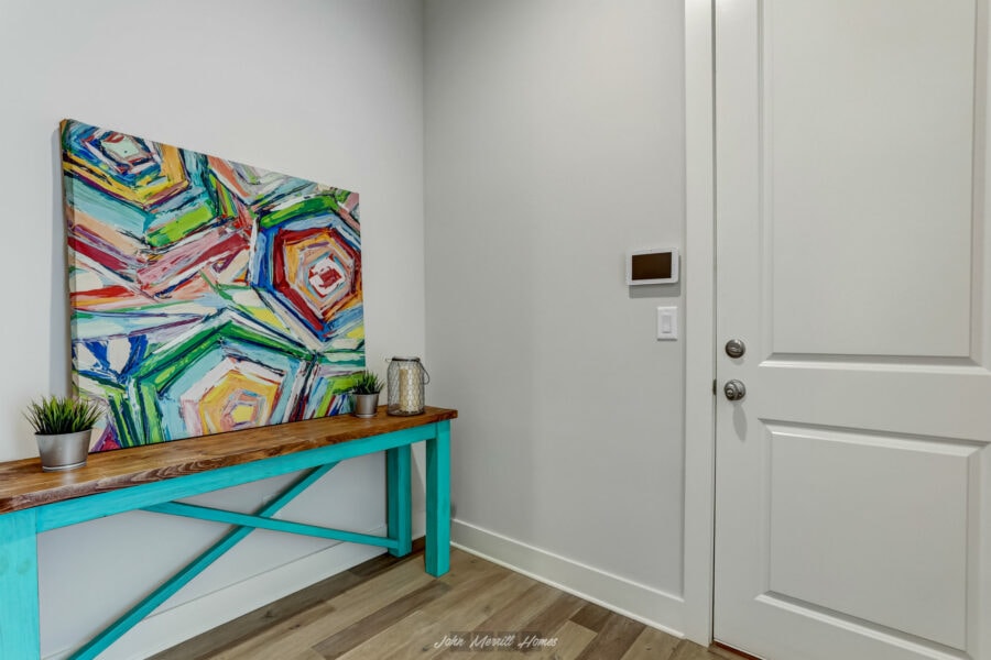 Bright entryway with a colorful abstract painting, small potted plants, and decorative lantern on a wooden console table in a modern home interior.