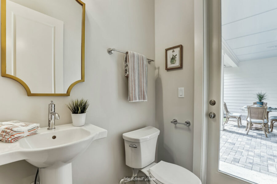 Comfortable modern bathroom with a white pedestal sink, a small potted plant, a framed wall art, a striped towel on a chrome towel bar, and a glass door leading to an outdoor patio with outdoor furniture.