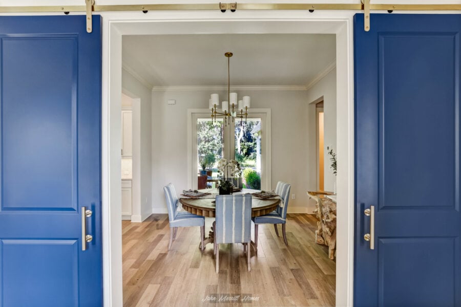 Modern dining room with a round wooden table, six cushioned chairs with striped fabric, hardwood floors, and a window with garden view, in a contemporary home interior.