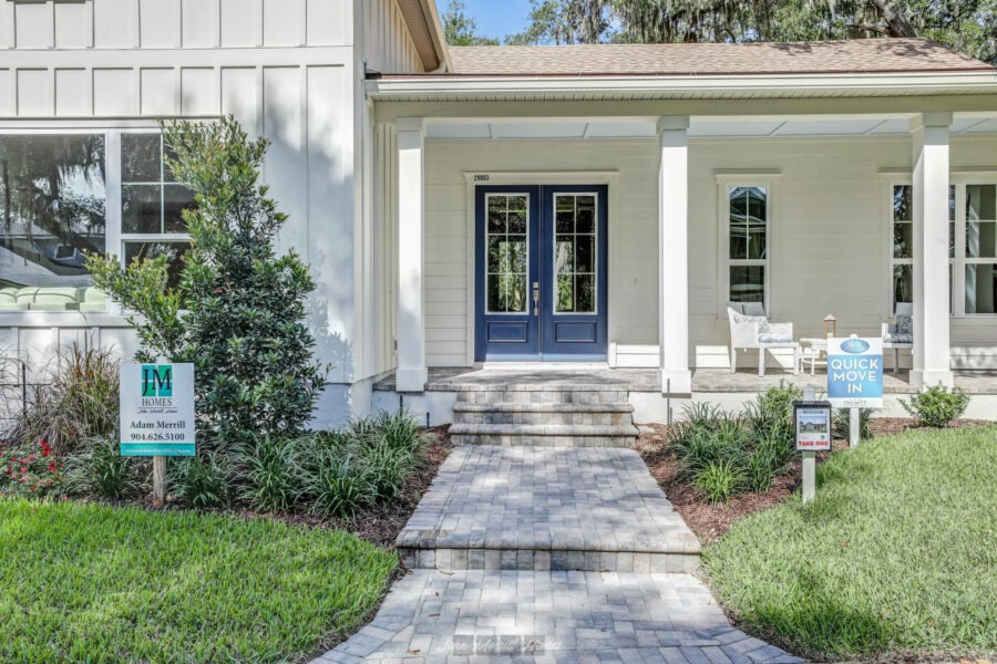 Elegant white house entrance with a vibrant blue double door, surrounded by lush greenery and a neatly paved walkway, showcasing modern residential architecture.