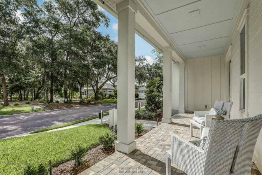 Comfortable front porch with white wicker chairs, landscaped yard, and mature trees, offering a welcoming setting for relaxation and outdoor enjoyment.