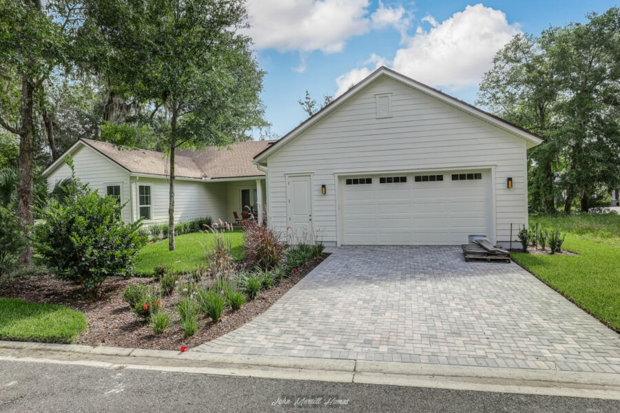 Modern white farmhouse-style home with landscaped front yard, paved driveway, and attached garage in a lush green setting.