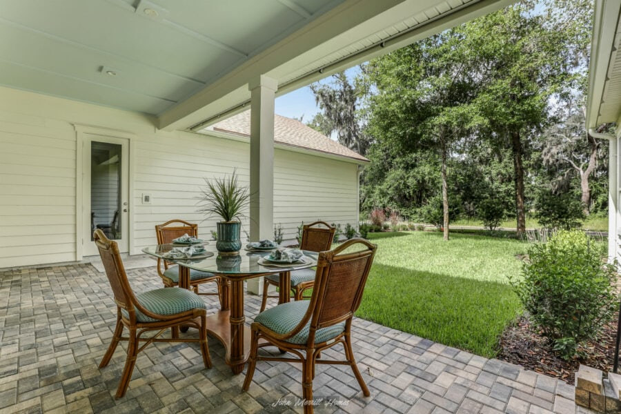 Enjoy a charming outdoor covered patio with a glass-top dining table, comfortable wicker chairs, and lush green backyard scenery, perfect for relaxing and entertaining.