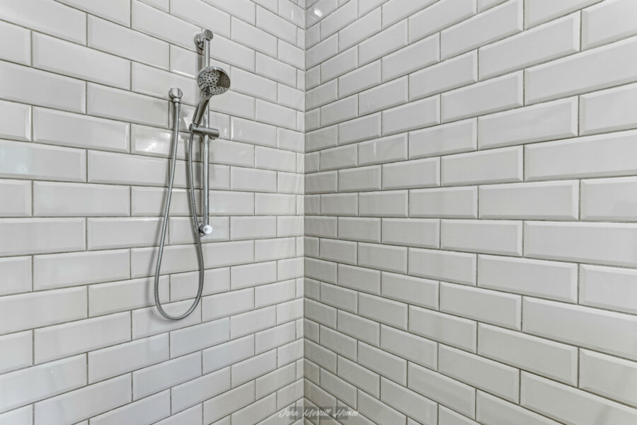 Shower with white subway tiles and stainless steel fixtures in a modern bathroom.