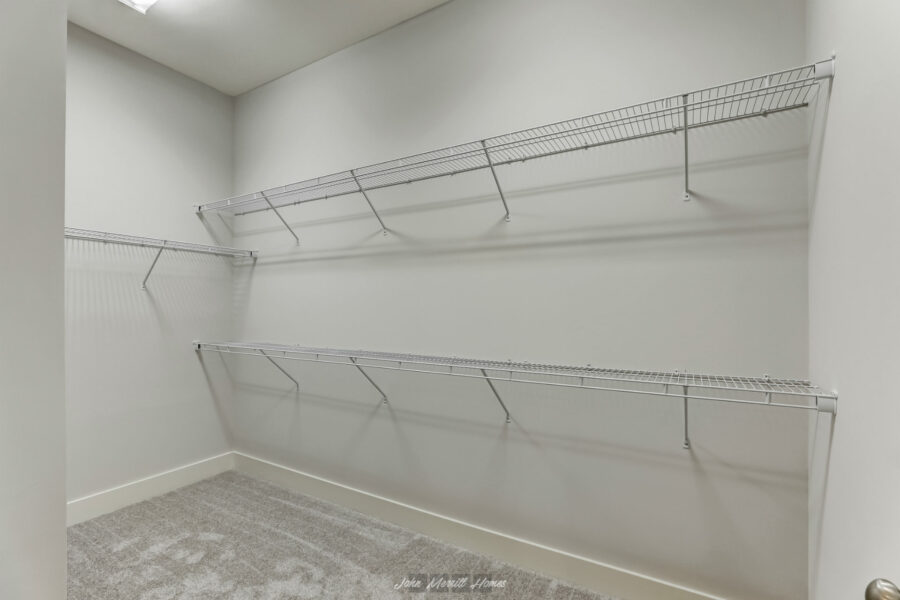 Storage closet with white wire shelving and gray carpet flooring, interior space for organizing clothing and accessories.