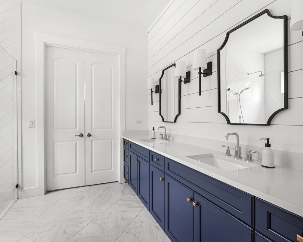 Contemporary bathroom vanity with white countertops, navy-blue cabinets, black-framed mirrors, and modern black wall sconces. Features dual sinks, sleek fixtures, and a spacious design for elegance and functionality.