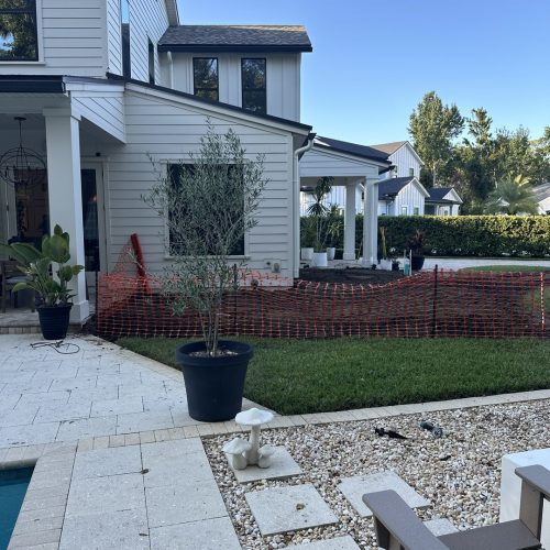 Stylish white modern home exterior with a landscaped backyard, potted plants, a small tree, decorative mushroom sculpture, and a cozy sitting area, reflecting quality craftsmanship by John Merrill Homes.