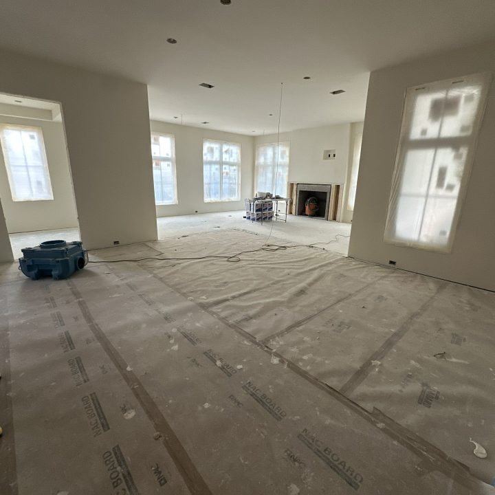 Spacious living room under construction with large windows, neutral walls, and an unfinished fireplace, showcasing modern interior design and upcoming home finishes.