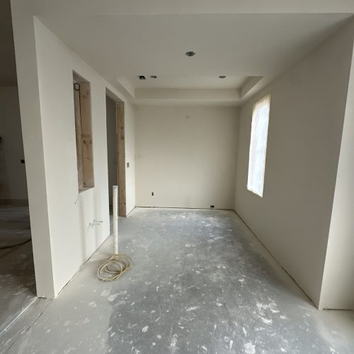 Bright interior of a new, unfinished home under construction, showing freshly painted walls, exposed wiring, and a window with natural light. The space is ready for flooring and final fixtures.