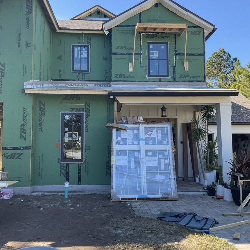 1. New two-story house under construction with green weather-resistant sheathing, multiple windows, and a front porch with landscaping.