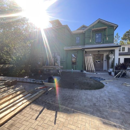 1. New two-story house under construction with green sheathing and partially finished exterior in a sunny residential neighborhood.