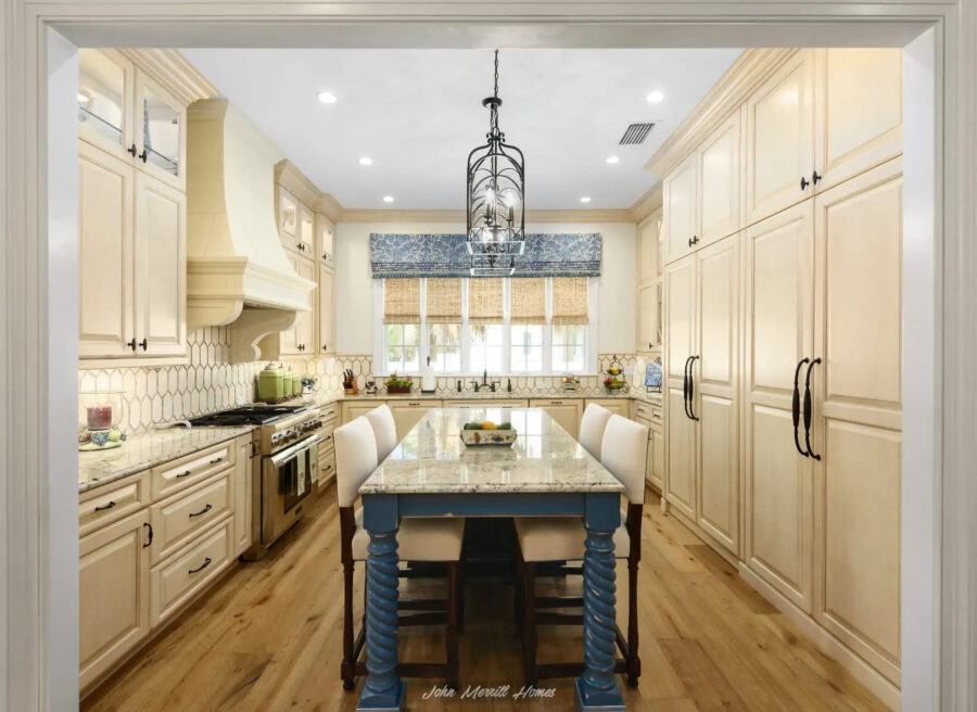 Bright, spacious kitchen with cream cabinets, a large island with a blue base, and a central chandelier.