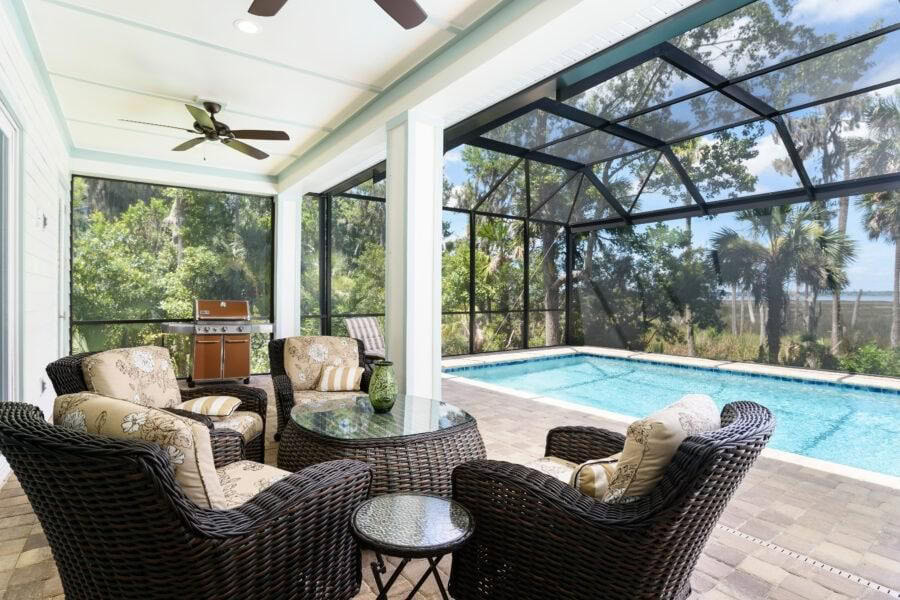 Bright screened-in porch with seating area and pool, surrounded by lush greenery and trees.