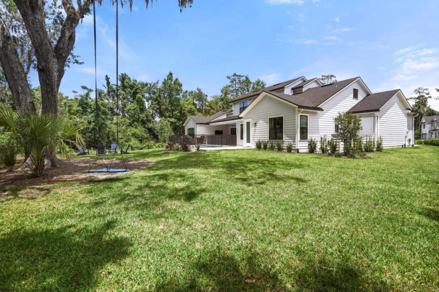 Spacious modern white house with large backyard, lush green lawn, and mature trees, showcasing a beautiful residential property.