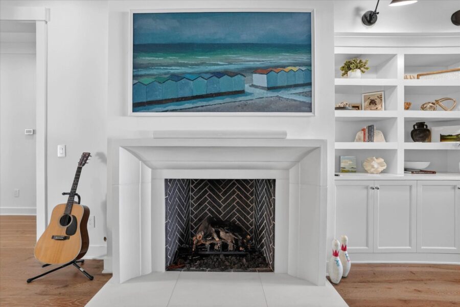 Elegant white fireplace with a colorful landscape painting above and built-in white shelving units on either side, decorated with books, vases, and decorative objects, creating a cozy and stylish ambi.