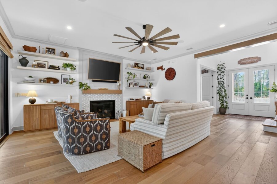 A spacious, bright living room featuring a cozy fireplace, large windows allowing natural light, and stylish furniture including a sofa and armchairs.